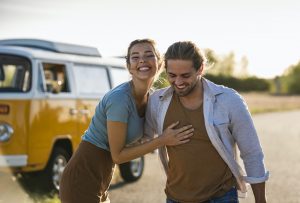 Happy couple doing a road trip with a camper, embracing on the road