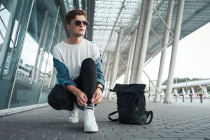 Casual young guy ties his shoelaces near the airport terminal