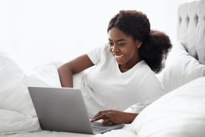 Cheerful african american lady surfing on Internet in bed